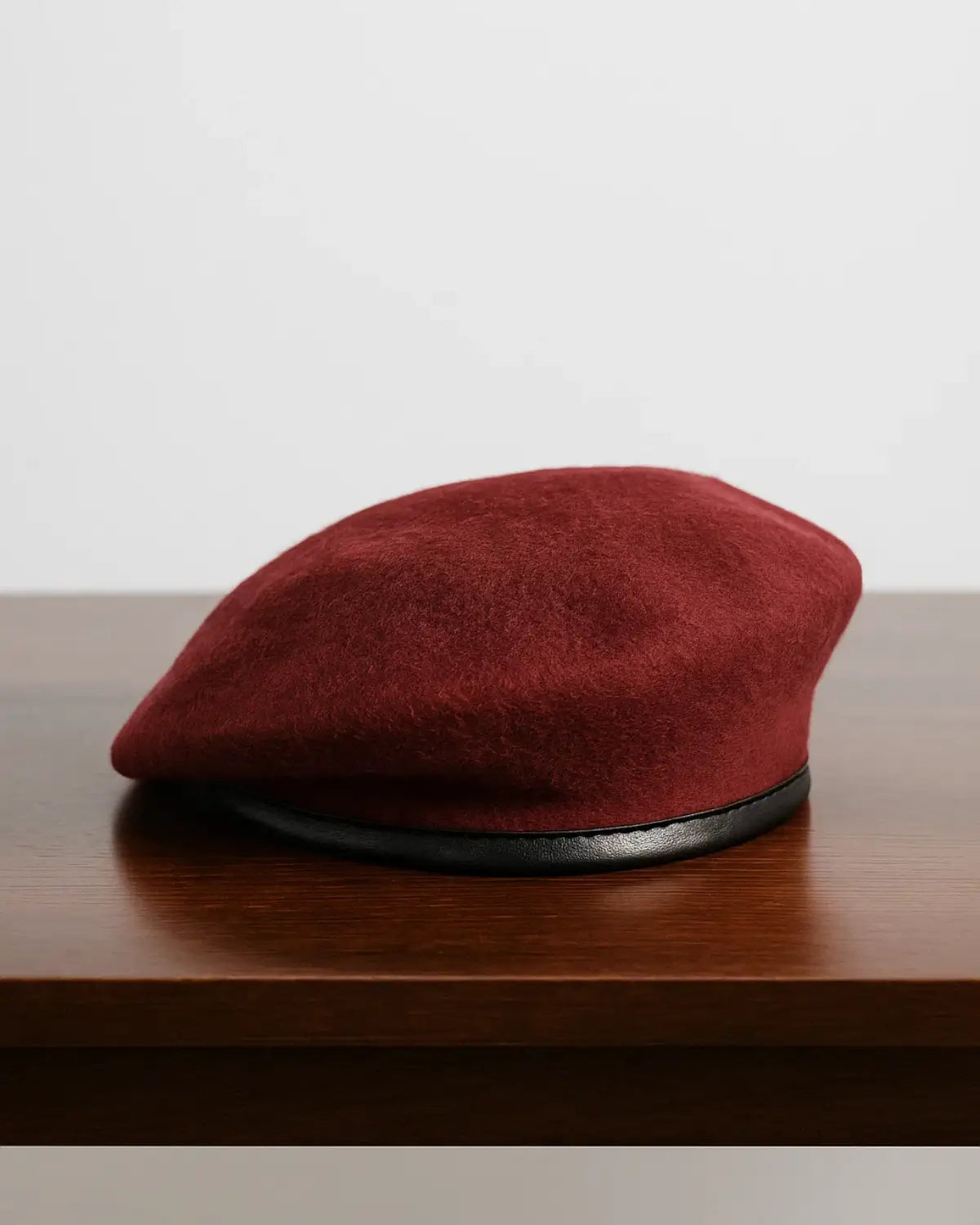 Boina masculina francesa de lã ajustável na cor vinho sobre mesa de madeira escura, destacando textura premium e acabamento sofisticado.


