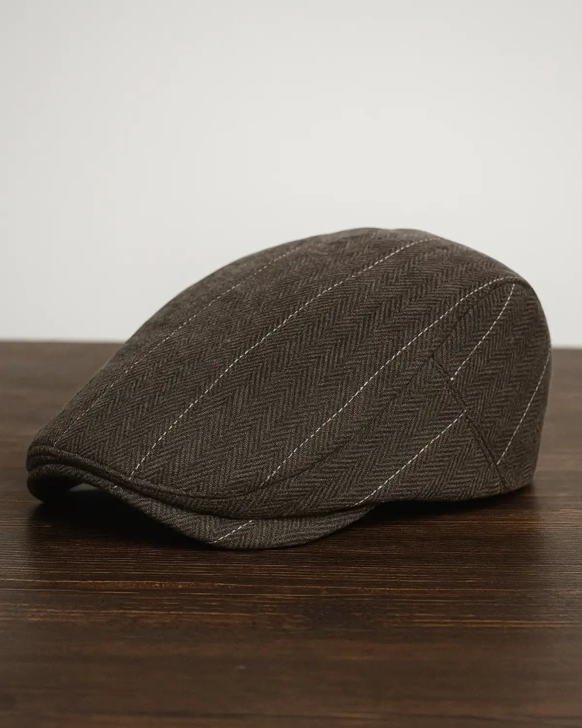 Boina inglesa masculina de algodão marrom com padrão clássico em cima de uma mesa de madeira escura.