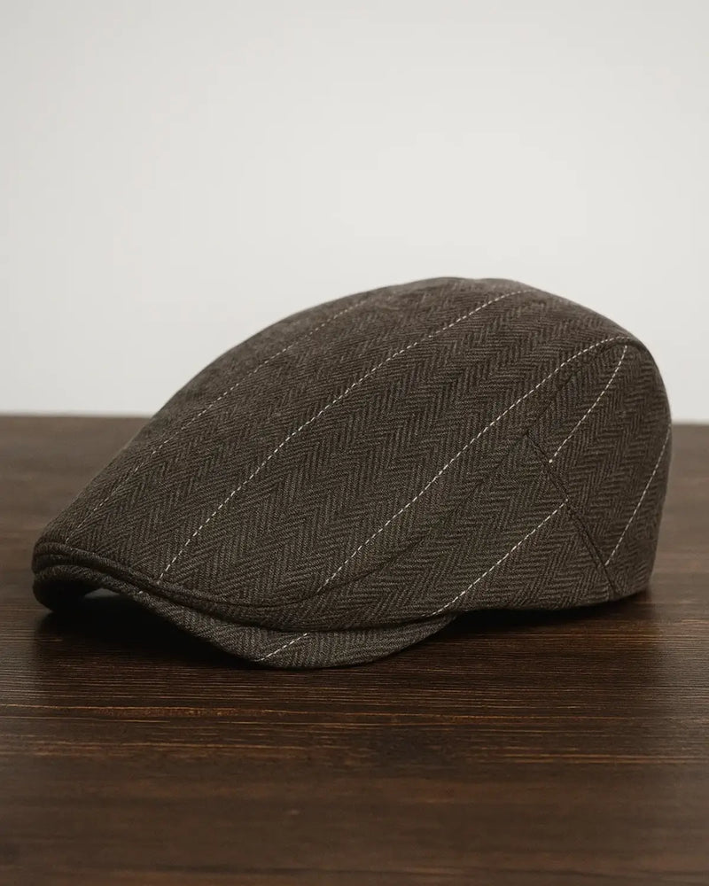 Boina inglesa masculina de algodão marrom com padrão clássico em cima de uma mesa de madeira escura.