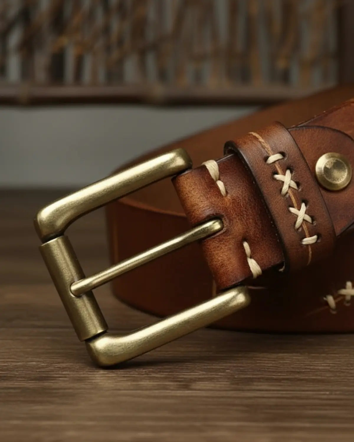 Detalhe fivela cinto masculino couro legítimo Mercer Khaki, costura clara, acabamento premium artesanal sobre mesa de madeira