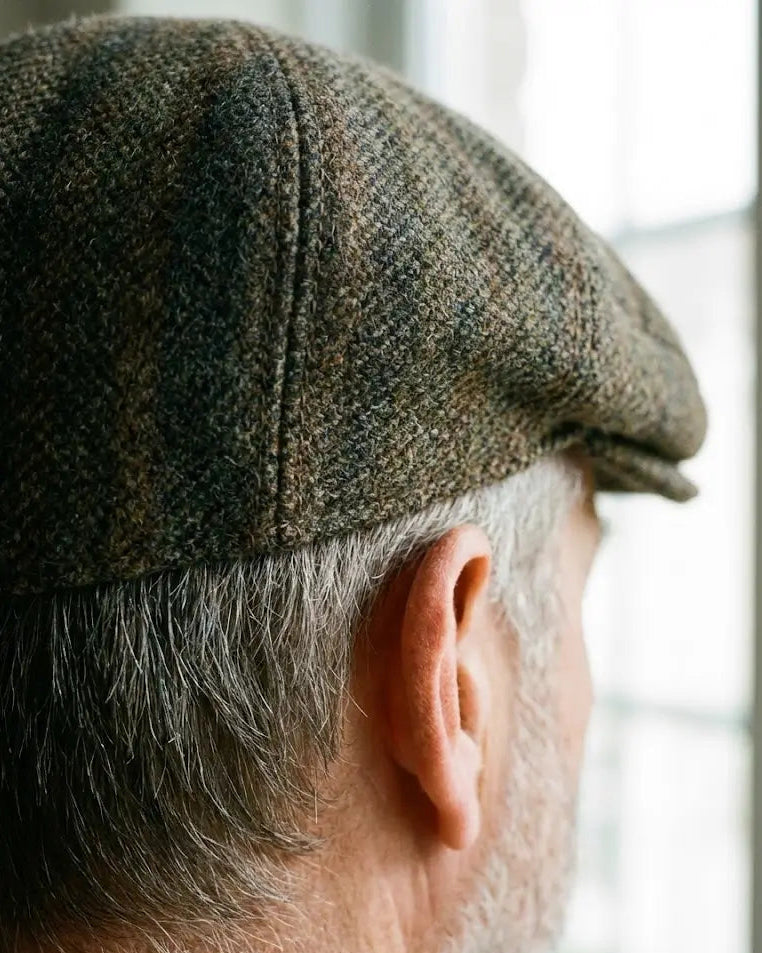 Detalhe aproximado (macro) da parte traseira de uma boina inglesa de tweed cinza. Mostra o caimento anatômico na nuca e a costura reforçada, garantindo conforto sem apertar a cabeça. Acabamento de alfaiataria premium