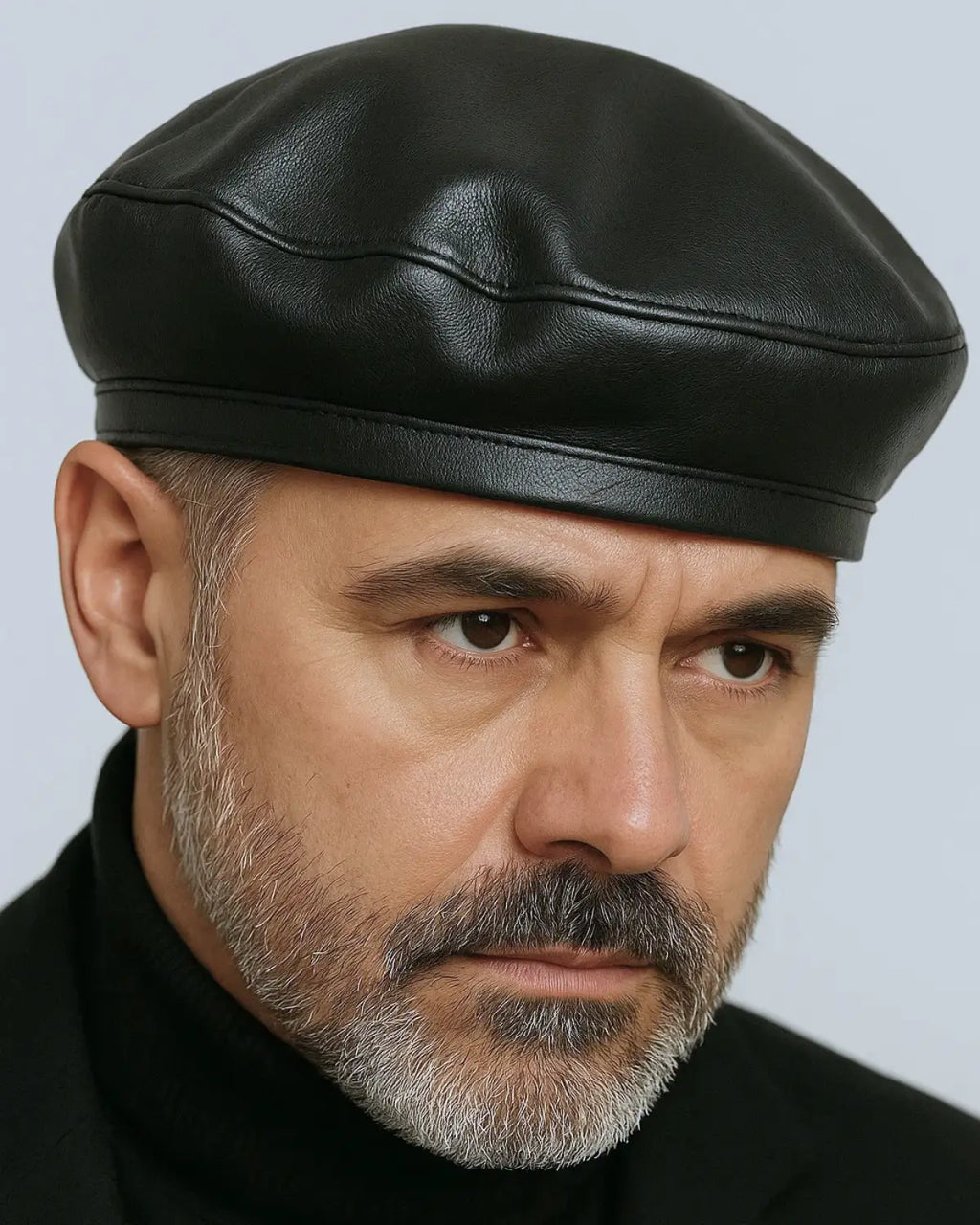 Close frontal de homem usando boina masculina francesa em couro preto, expressão séria e barba grisalha