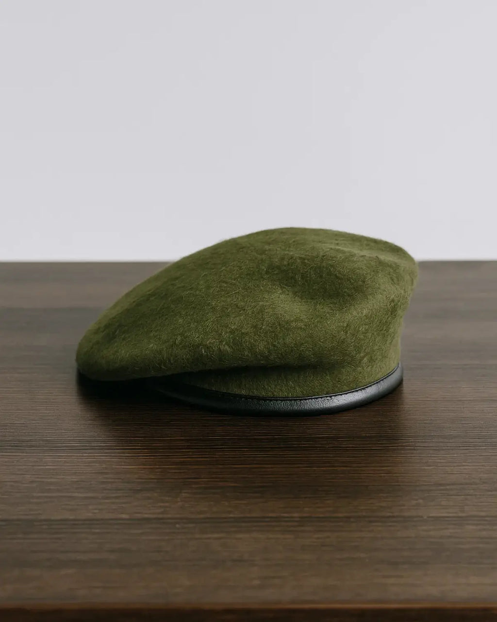 Boina Masculina Francesa de Lã Ajustável na cor Military Green sobre mesa de madeira escura, estilo clássico atemporal