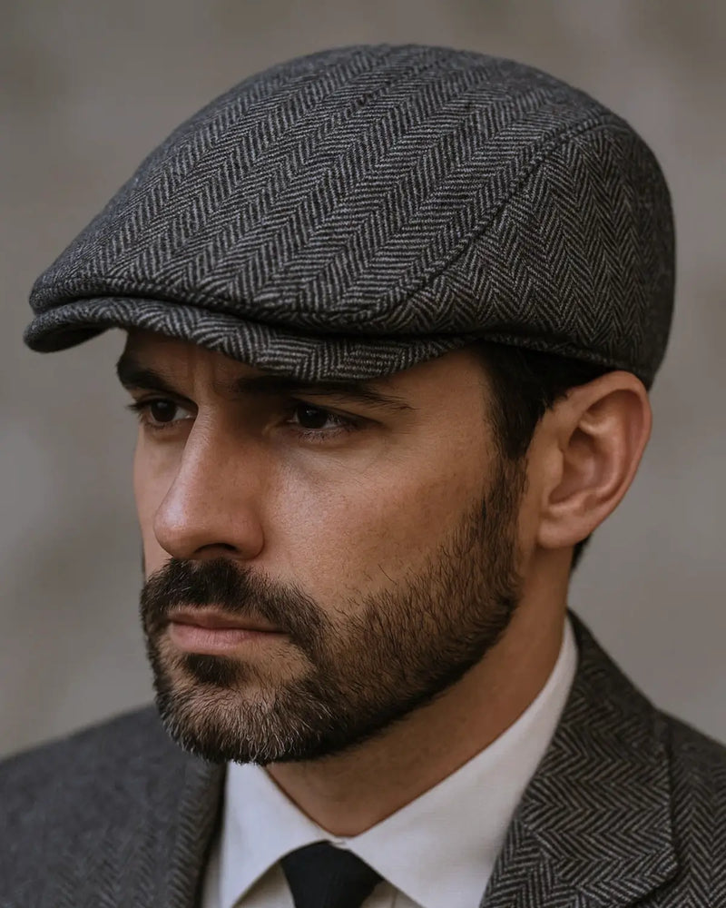 Close de jovem com boina inglesa masculina cinza e terno, destacando o estilo sofisticado do acessório.