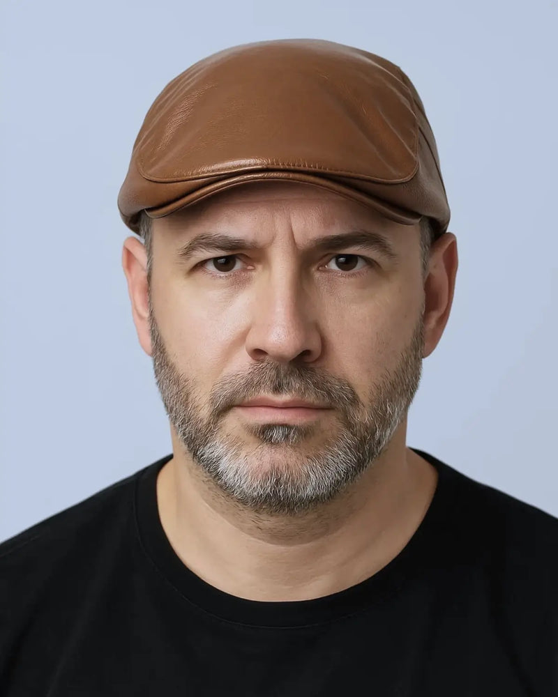 Retrato frontal de homem com boina inglesa marrom e expressão séria, fundo neutro claro