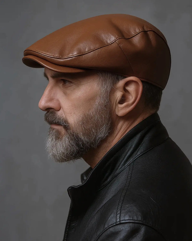 Close de perfil de homem com boina inglesa marrom e jaqueta preta, fundo acinzentado editorial