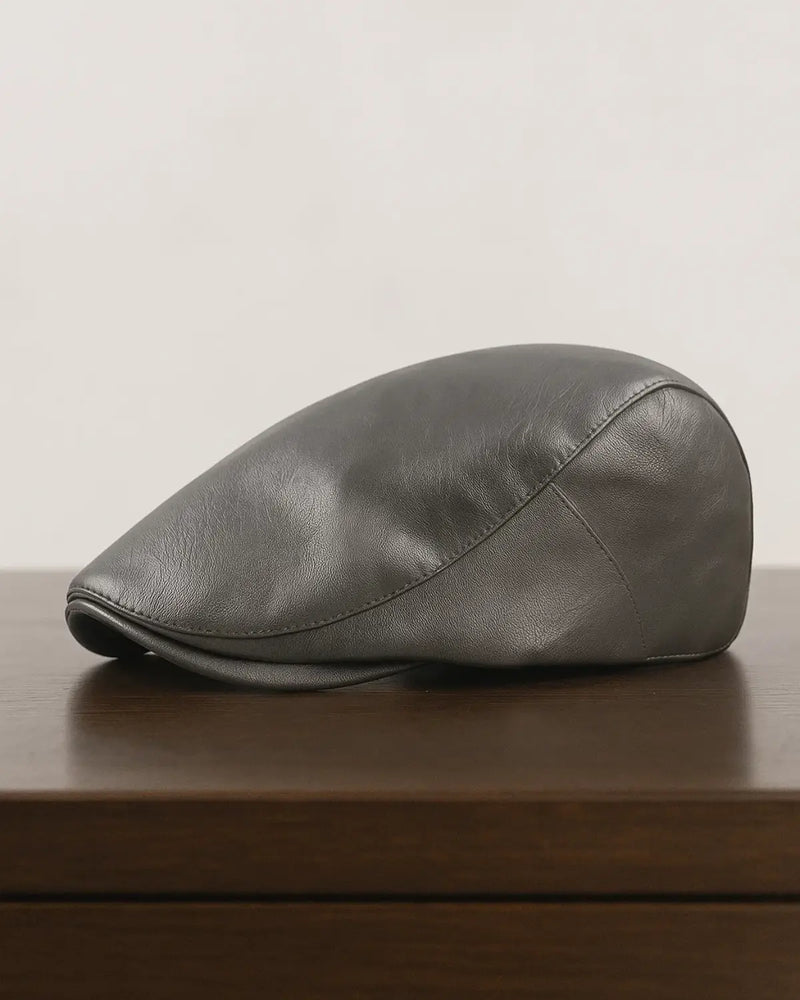 Boina masculina inglesa cinza em couro sintético posicionada sobre mesa de madeira escura