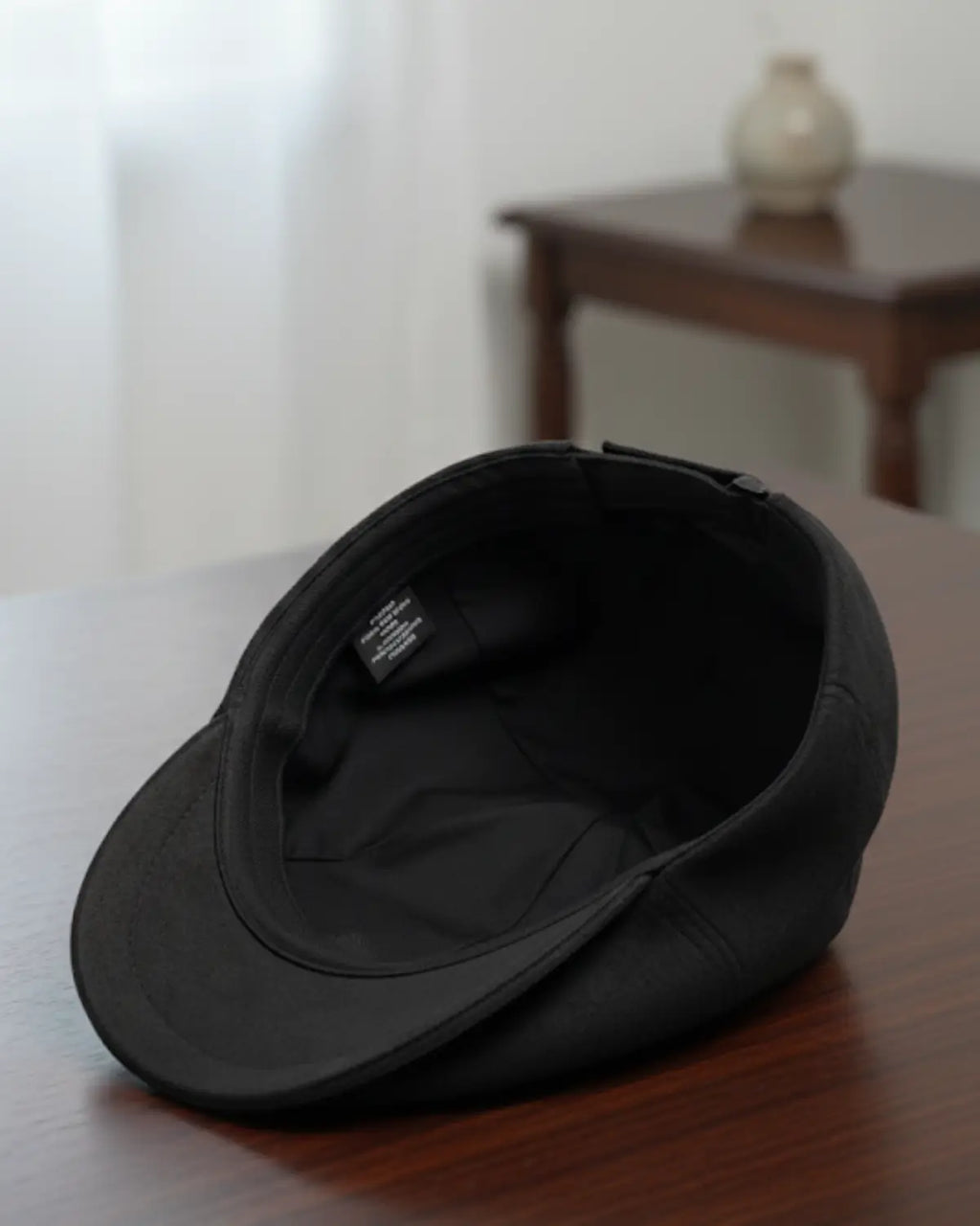 Forro interno e acabamento da boina masculina inglesa em couro vegano preto, sobre mesa de madeira, qualidade e sofisticação Cappel