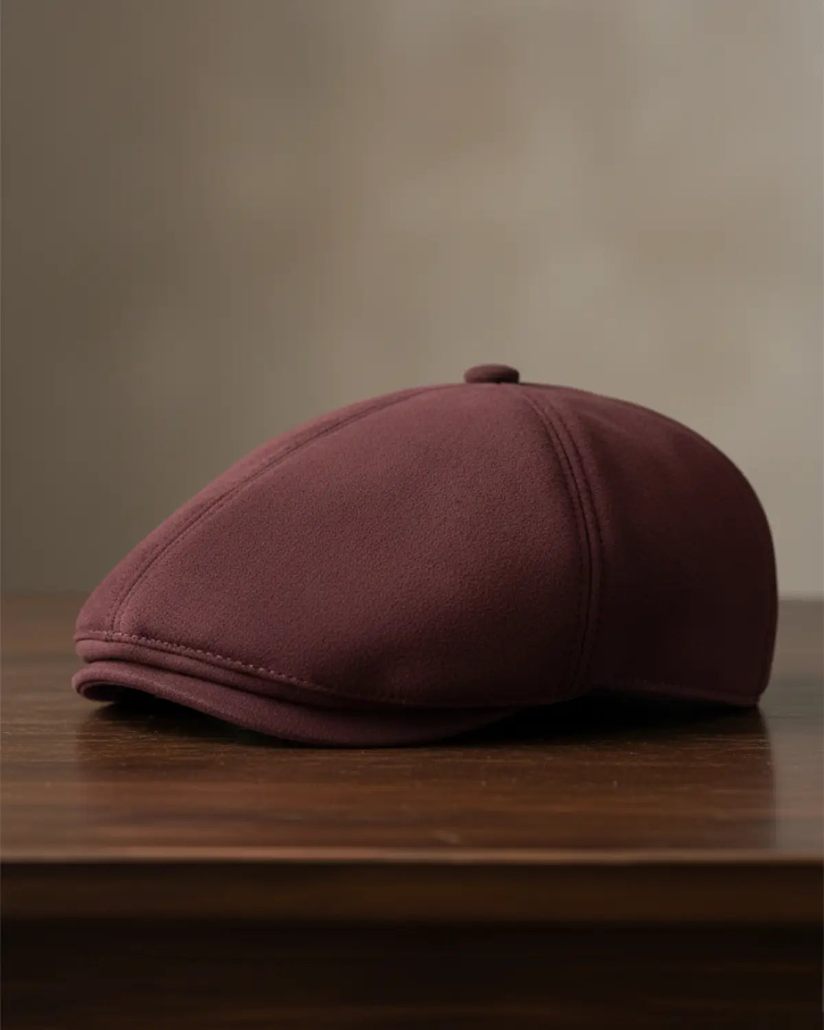 Boina masculina inglesa burgundy em couro vegano vista de perfil sobre mesa de madeira escura, acessório premium masculino, editorial sofisticado.