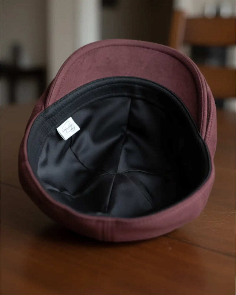 Forro interno e acabamento da boina inglesa burgundy em couro vegano, sobre mesa de madeira, alta qualidade e conforto