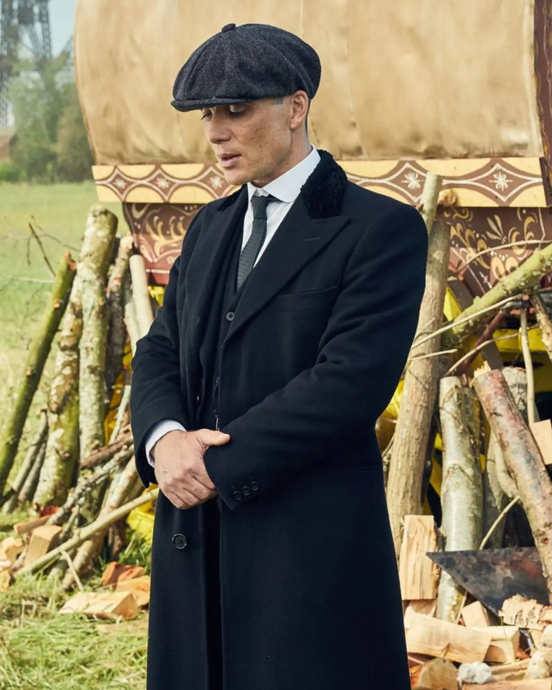 Thomas Shelby usando Boina Peaky Blinders Newsboy em um look de inverno elegante e sóbrio com sobretudo preto em ambiente externo.