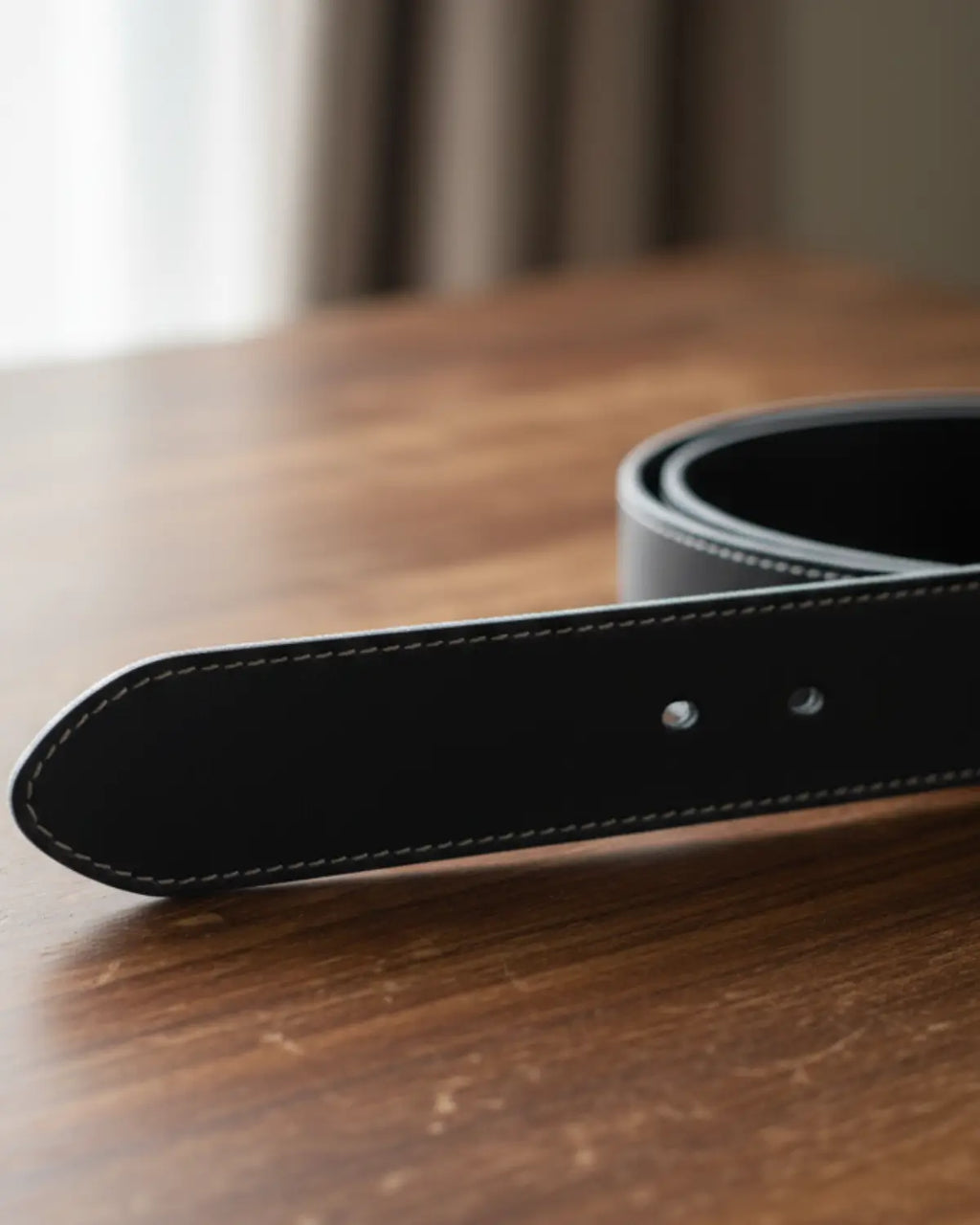 Detalhe da ponteira do cinto masculino de couro legítimo preto com costura clara sobre mesa de madeira