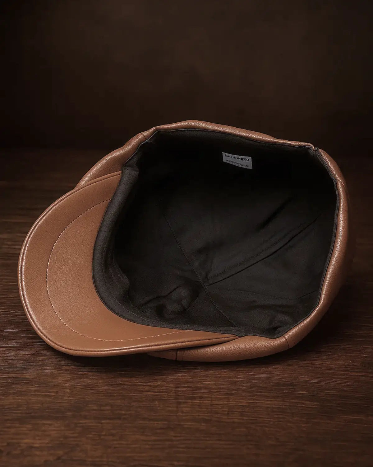 Visão interna da boina masculina italiana de couro marrom com forro preto e aba estruturada sobre mesa de madeira escura
