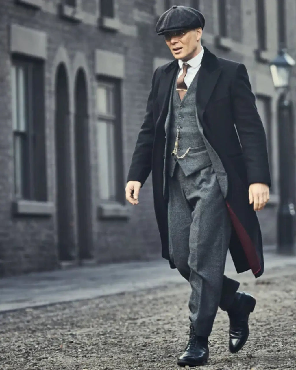 Inspiração de visual Peaky Blinders: Thomas Shelby caminhando na rua vestindo boina Newsboy cinza chumbo, terno de três peças e sobretudo longo.